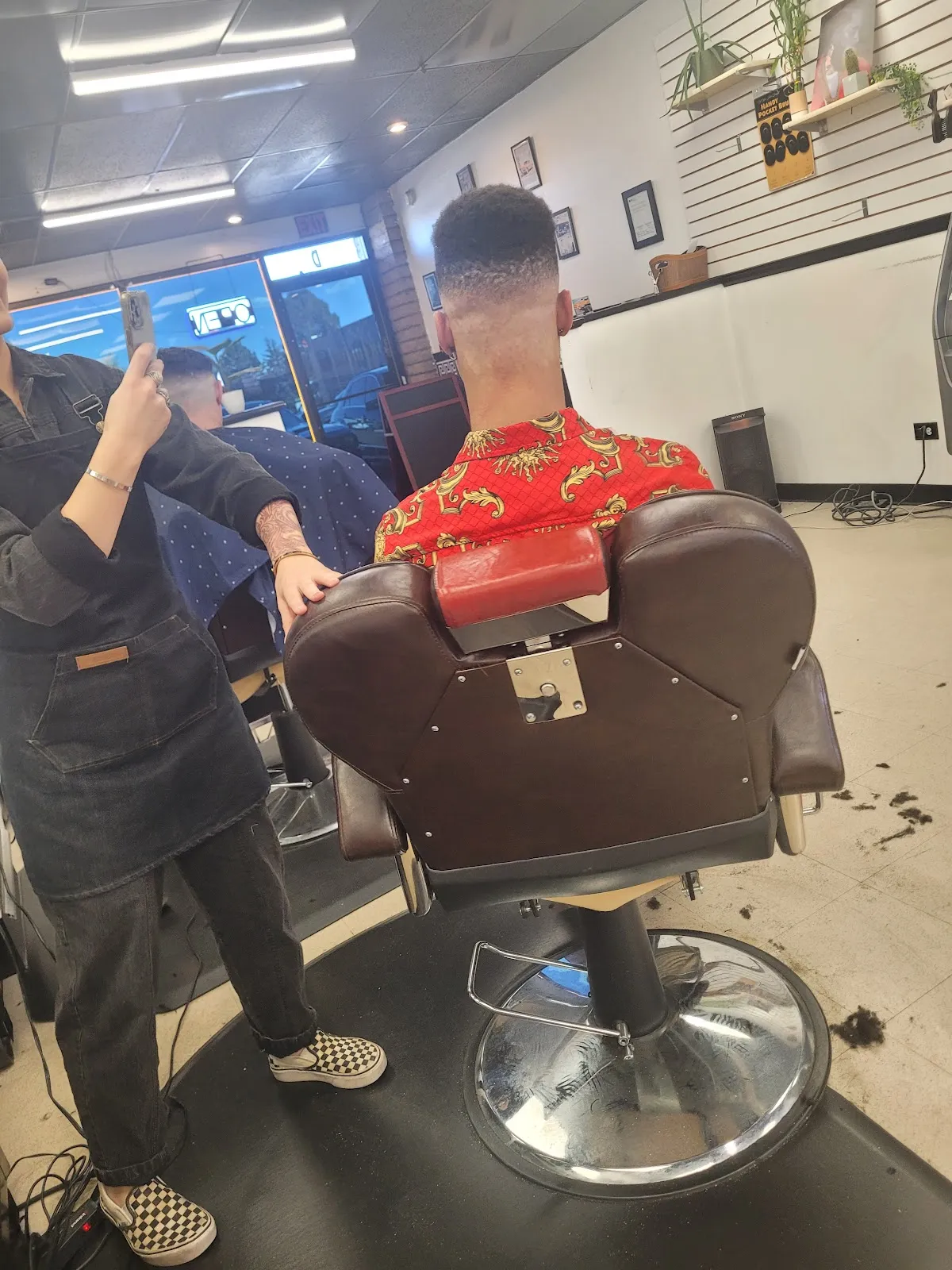 Inside the shop: a fresh skin fade in progress in a brown-leather barber chair against a white slat wall with plants