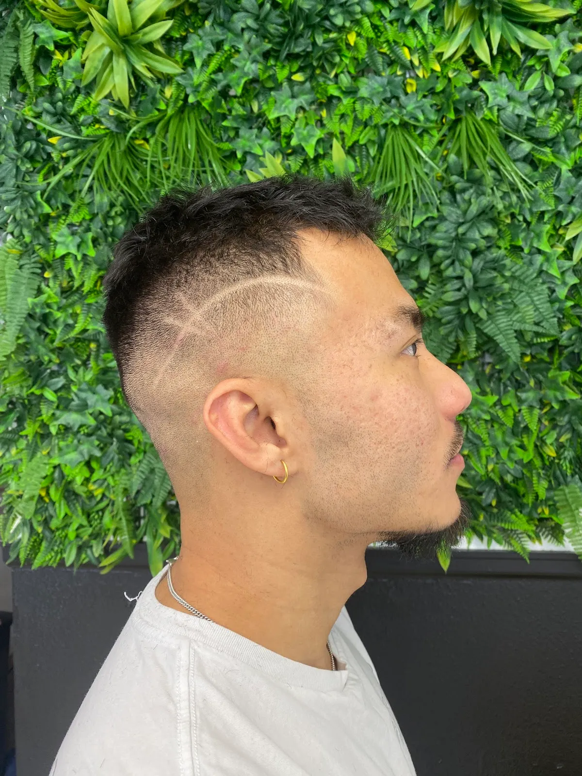 A finished skin fade with a sharp hair design, shown against the shop's green plant wall